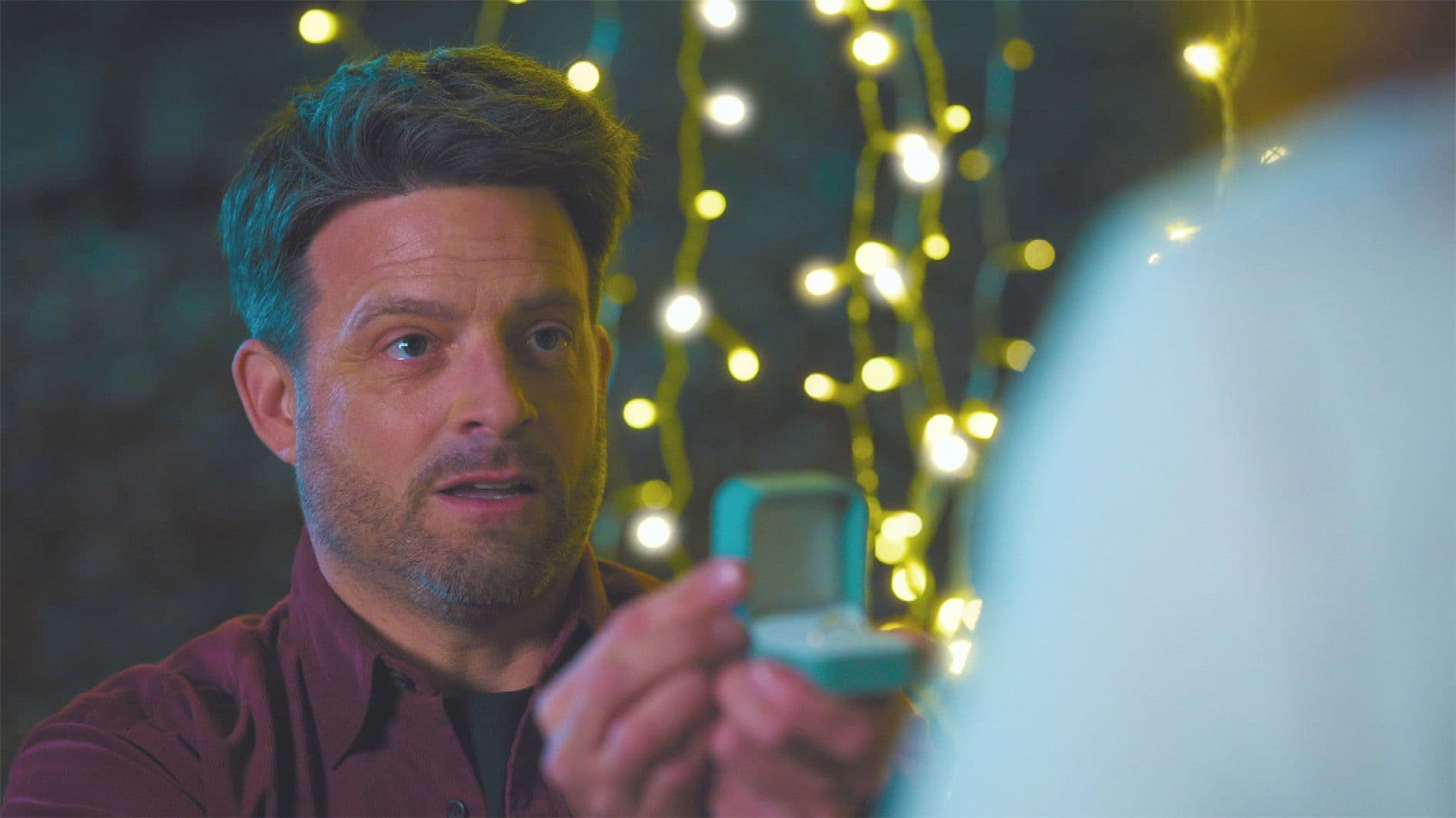 Erik (Daniel Buder) geht auf die Knie und hält eine Ring-box in die Hand. Dabei schaut er aufgeregt zu Lea hoch.